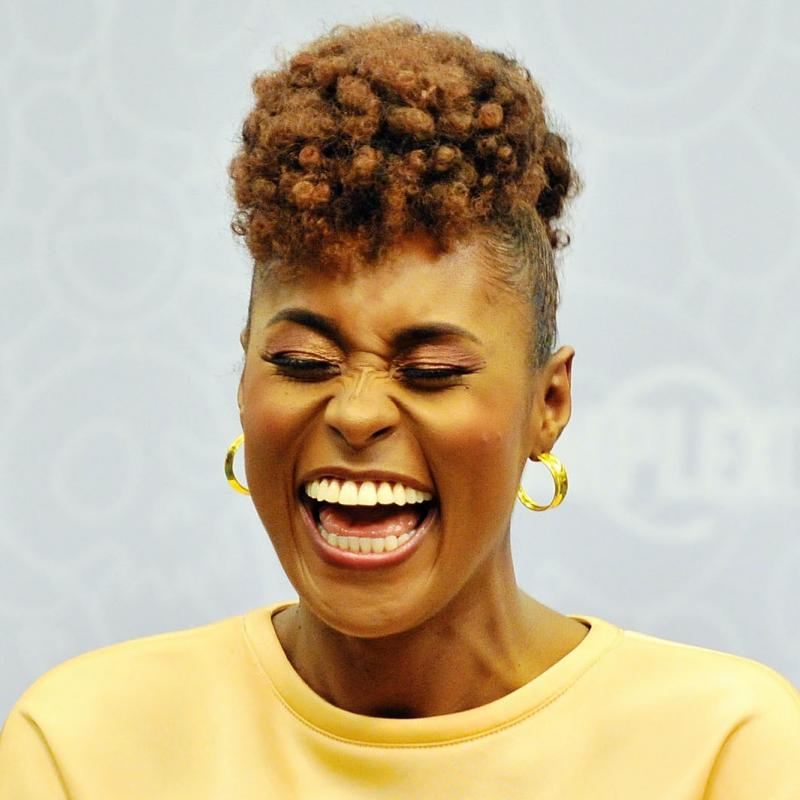 Issa Rae laughs while wearing a yellow sweatshirt